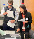 Two people , one wearing goggles, reviewing documents in a workshop.