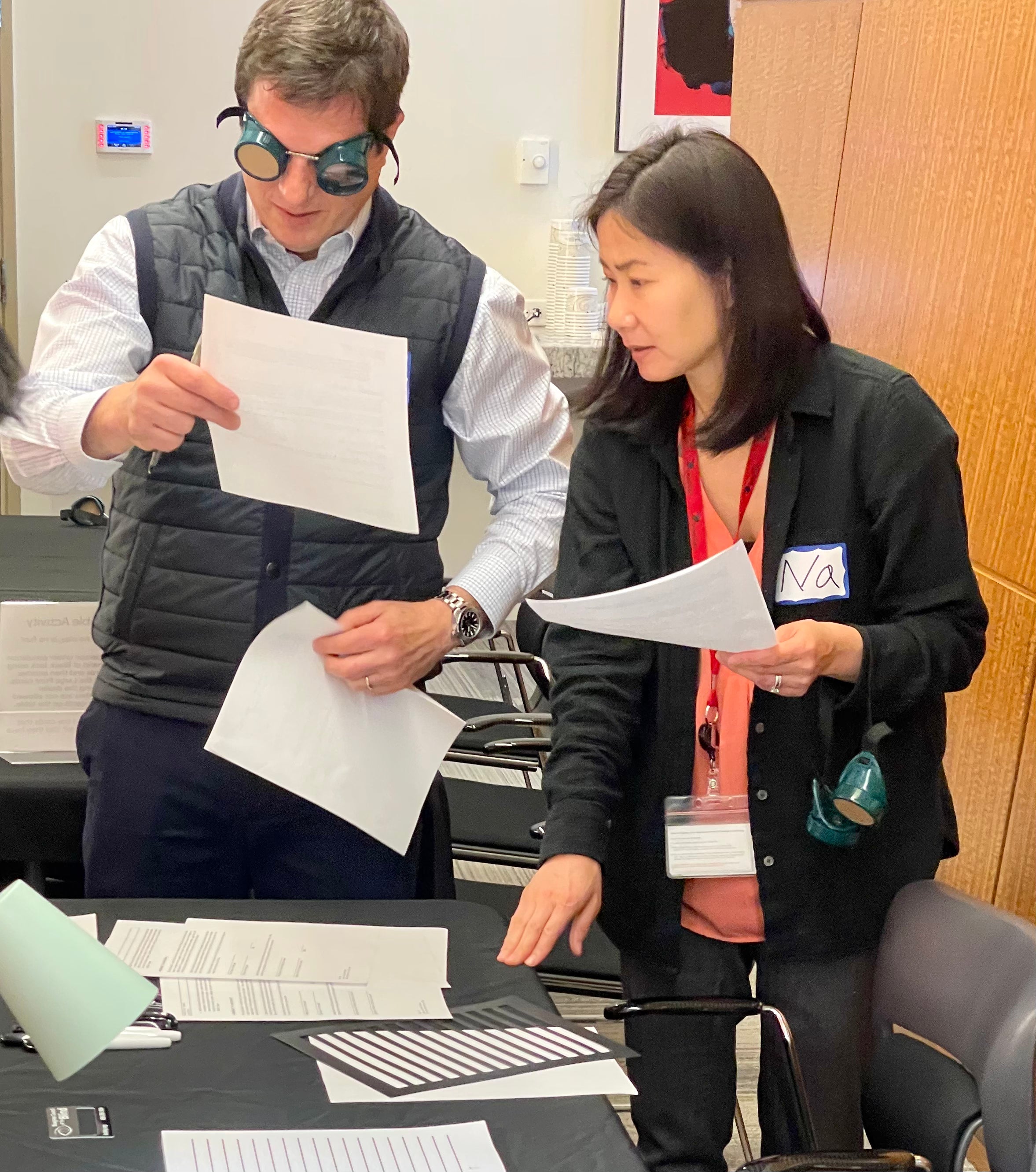 Two people , one wearing goggles, reviewing documents in a workshop.