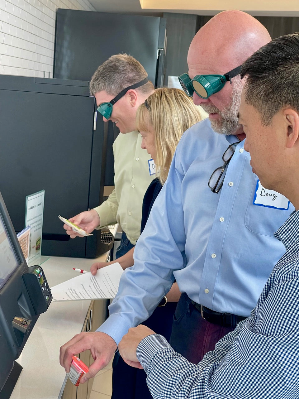 Four people, three men and a woman, are looking at a vending machine using simulation goggles.